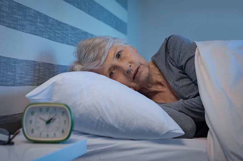 Older lady lying awake in bed, looking at her clock